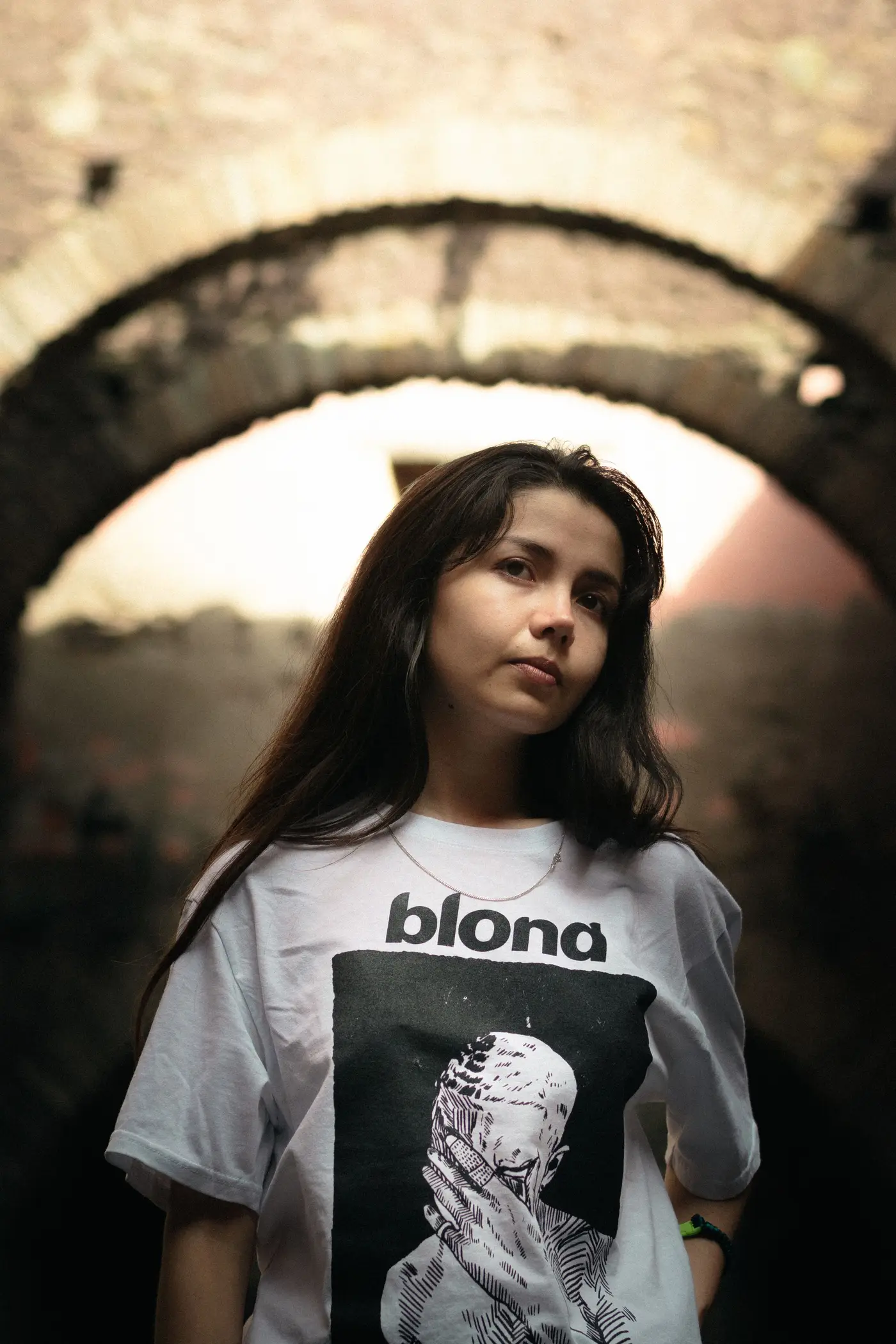 A person in a graphic t-shirt under a stone archway